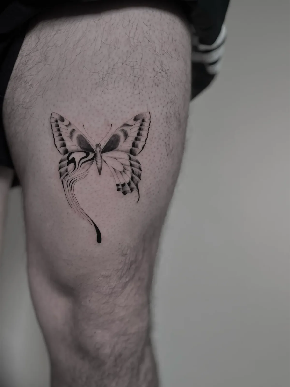 Illustrative blackwork butterfly with a liquid tail on the thigh, GAR Tattoo